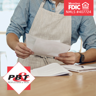 Business owner with apron on reviewing paperwork at desk in front of laptop at his business
